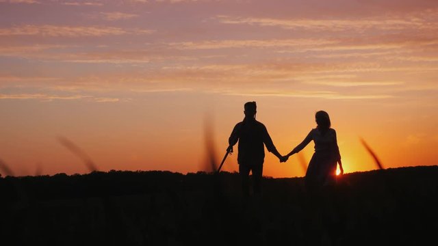 A young couple of farmers walking across the field to meet the camera. Silhouettes at sunset