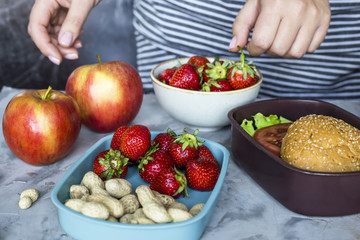 A woman's mother prepares her child for lunch in school and puts a sandwich and strawberries with...