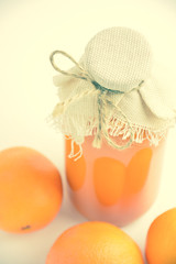 Glass transparent bottle with orange juice, close by there are three oranges. On a light background