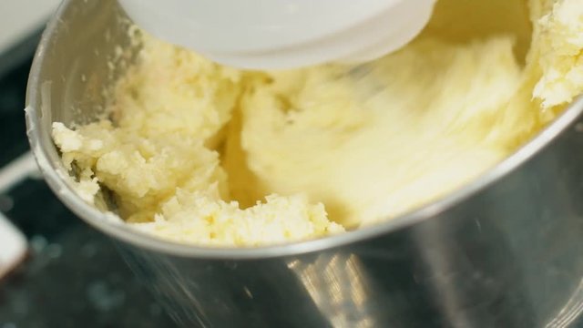Process of preparing dough using kitchen processor in kitchen indoors. Electric mixer stirs yellow mass for baking in bowl on table in cuisine. Metal nozzle rotates, stirring sweet duff. Concept