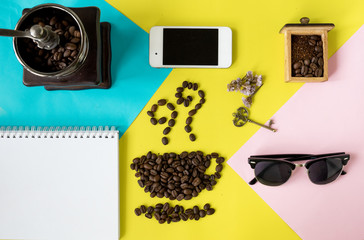 top view flat layer coffee beans in cup and smell icon shape, with vintage wooden coffee grinder, phone,  sun glasses and blank book on tree tone multicoloured background