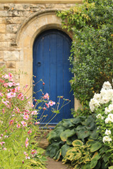 Vertical Image of blue door in a garden surrounded by flowers