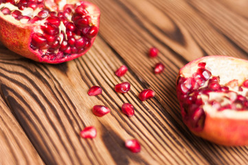 Scattered fresh ripe red seeds of pomegranate near two half pomegranate on old brown weathered wooden planks