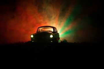 Fototapeta na wymiar Silhouette of old vintage car in dark foggy toned background with glowing lights in low light, or silhouette of old crime car dark background.