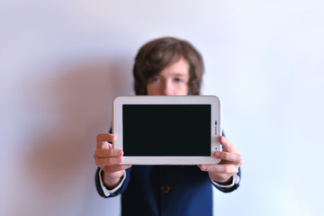 The schoolboy holds the tablet on his arms outstretched. The tablet is in the hands of a schoolboy.
