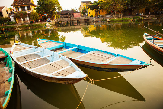 HOI AN, QUANG NAM, VIETNAM, April 26th, 2018: Boats by the river in ancient town Hoi An with view of typical yellow houses