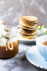 A pile of fritters next to a cup of tea and a jar of honey on a gray background among the flowers of the acacia. Spring delicious breakfast