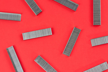 Scattered stationery new metal clips for stapler on red background. Top view