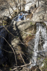 Mujer joven morena con pelo largo y liso sentada delante de una cascada