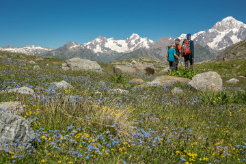 Naklejka premium Friends on a trip to the Italian Alps. Teen and a little boy trekking on a beautiful summer day during mountain holidays. A mountain panorama with three brothers walking with backpacks with snow-cappe
