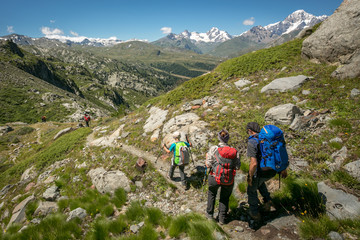 Fototapeta na wymiar A family on a trip to the Italian Alps. Father, mother and son trekking on a beautiful summer day during mountain holidays. A mountain panorama with a family walking with backpacks with snow-capped pe