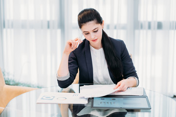 business analyst studying report papers with graphic results of company activity. information processing and data analysis concept. young professional woman at work