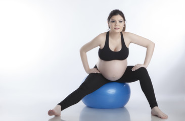Obraz premium Pregnant woman is doing exercises with gymnastic ball on white background