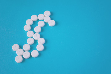 Top view of a white pills are laid out in the shape of a dollar symbol on a turquoise background with copy space (concept)