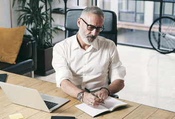 Attractive and confidental adult businessman using mobile laptop computer while working at the wooden table at modern coworking office.