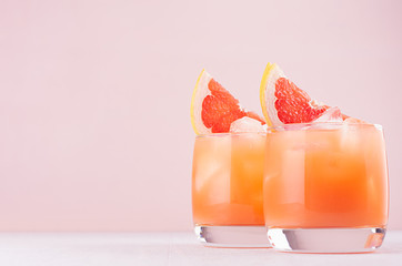 Cocktail de pamplemousse froid dans deux verres avec de la glace et des morceaux de pamplemousse sur fond rose pastel. Boisson diététique fraîche d& 39 été.