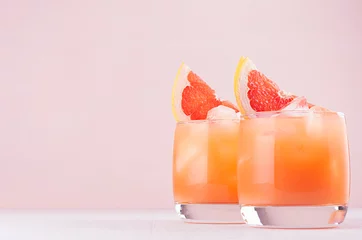 Wall murals Cocktail Cold grapefruit cocktail in two glasses with ice and pieces grapefruit on pastel pink background. Fresh summer healthy diet beverage.