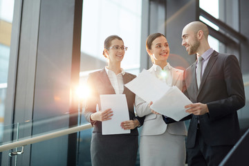 Three elegant brokers in suits discussing points of contract before negotiation with foreign...