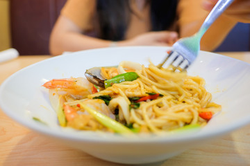 A Girl Eating Spaghetti in white plate on wooden Table.