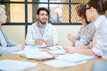Happy young businessman listening to ideas and opinions of his colleagues at working meeting
