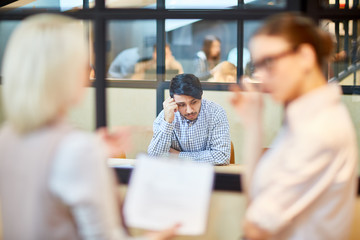 Pensive applicant sitting by table in boardroom and worrying before interview with employer