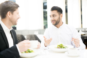 Fototapeta na wymiar Two elegant businessmen having talk in cafe or restaurant during lunch break