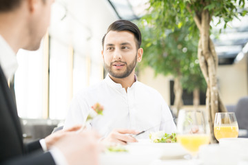 Confident young man and his business partner or colleague having talk by lunch in restaurant