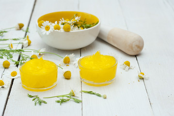 medical cream and daisy herbal flowers on white wood table background