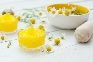 medical cream and daisy herbal flowers on white wood table background