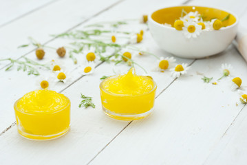 medical cream and daisy herbal flowers on white wood table background