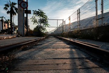 Primer plano de vías de tren abandonadas con sol de fondo y vegetación. Valla que corta el paso