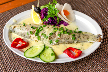 Fresh delicious trout in white creamy sauce, with vegetables on a white plate.