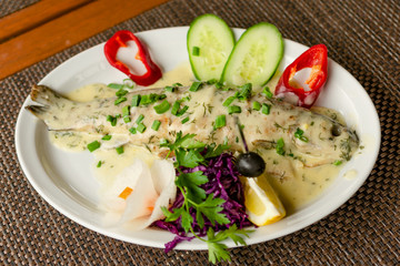 Fresh delicious trout in white creamy sauce, with vegetables on a white plate.