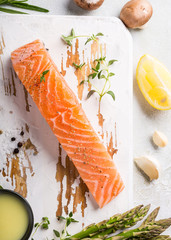 Overhead shoot with fresh green asparagus, raw salmon fillet, herbs and sauce and old white wooden board. Healthy food background, copy space, top view.