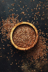 Flax seeds in a wooden bowl, brown background, top view