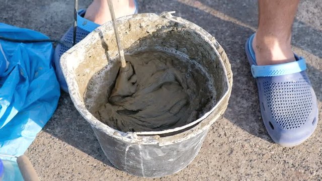 Close up shot of a builder mixing cement in a bucket on a constraction site with a special tools.