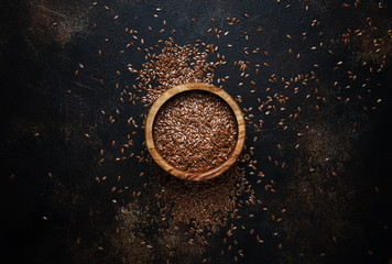 Flax seeds in a wooden bowl, brown background, top view