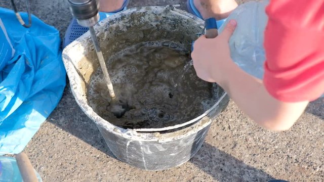 Close up shot of a builder mixing cement in a bucket on a constraction site with a special tools.