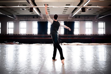 Back view silhouette of male ballet dancer practicing his skills on the stage. Dancer in epic pose. Backlight - contrast silhouette