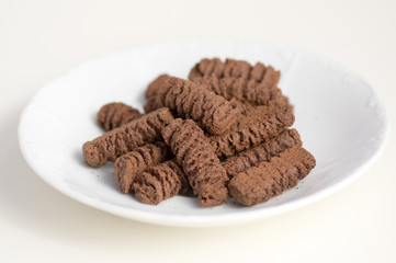 Dark brown cocoa tea biscuits on white plate, tasty unhealthy sweets