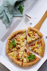 Pizza Hawaiian in a cardboard box on a light stone or concrete background. Pizza delivery.