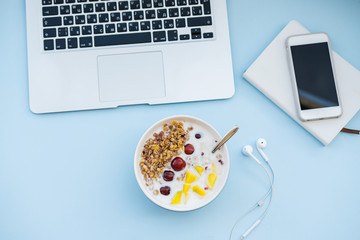Healthy breakfast before working. Bowl of homemade Granola baked with yogurt aand laptop on blue background