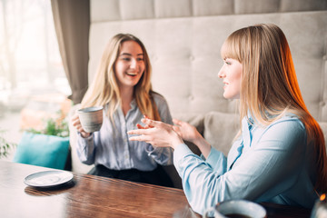 Two smiling girlfriends drinks coffee in cafe