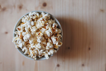 A bowl filled with popcorn placed on a light wooden table surface