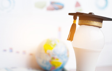 Graduate study or Education knowledge is power concept: Graduated cap Put on white light bulb and graph background. Conceptual for Educational is Navigation light for successs study or business world
