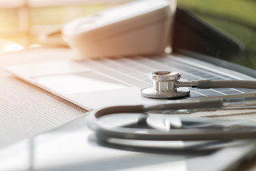 Stethoscope put on modern Laptop computer at wood table medicine doctor work office in hospital or clinic with light flare, Concept of Health Care and Medical. Selective focus.