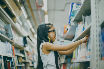 Little Asian child  picking books from the bookshelf