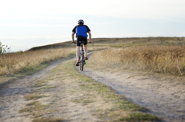 Fototapeta premium Male cyclist driving by rural dirt road outdoors