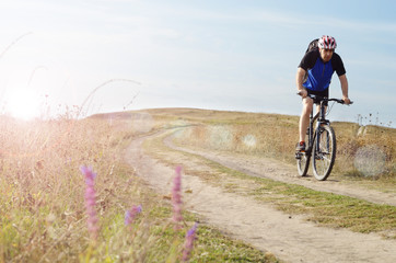 Obraz premium Male cyclist with backpack driving by rural dirt road outdoors