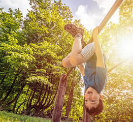 Happy child boy hanging upside  down on bar, playground in forest, outdoor activities